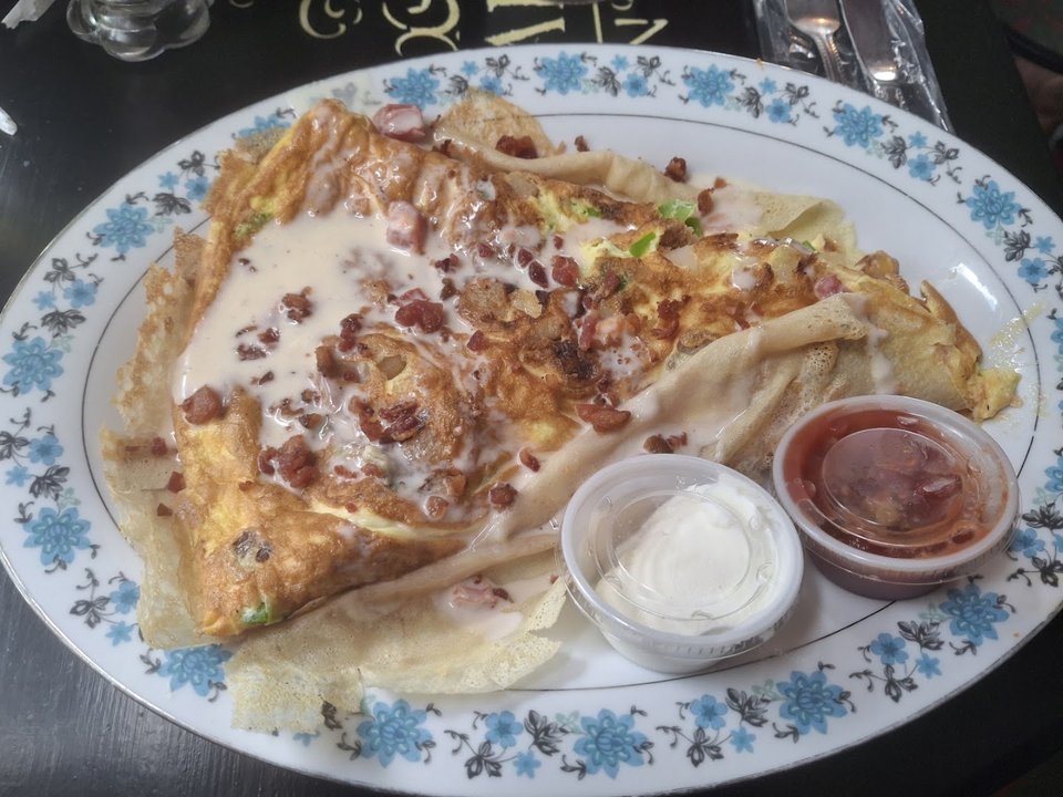 Coffee cups beside a sweet crêpe on a table.
